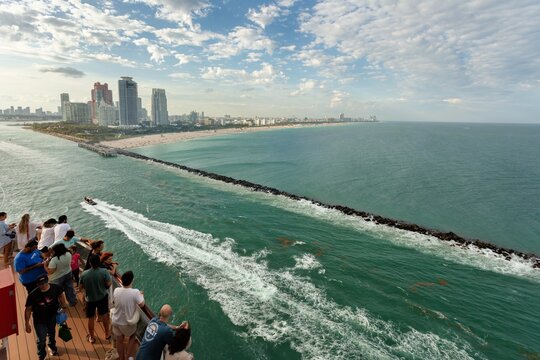 Miami, United States - 16 March 2026: View of Miami's towering skyline and a bustling beach, with vibrant turquoise waters and a rugged jetty under a dramatic sky.