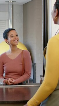 Shifting staff in yellow top and apron leaning on steel counter, greeting seated guest, copy space