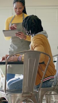 Vertical video: Walking server in apron showing tablet to seated customer in cafe, explaining menu