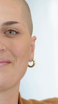 Vertical video: Smiling shaved woman widening mouth into laugh in studio wearing tan top, nose hoop