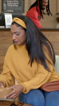 Vertical video: Tapping phone, woman in yellow top at cafe getting brown box for pickup, inspecting