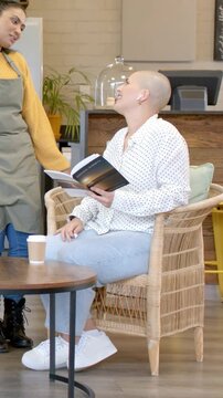 Vertical video: Reading woman with book in cafe, apron staff approaching on left, chatting, writing