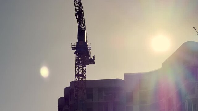 A dark crane stands guard over a concrete apartment structure under a hazy, golden sky. The warm light creates an inspiring and hopeful feeling of future growth.