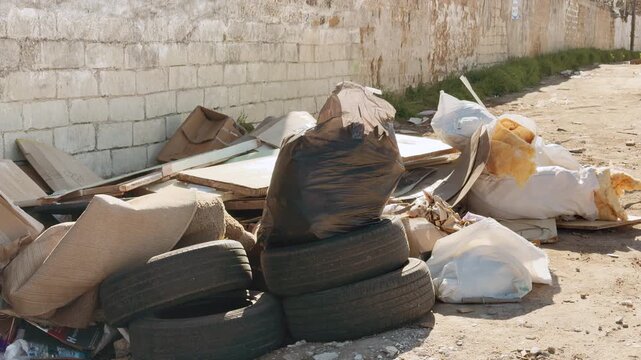 Old tires, black trash bags, and white sacks sit abandoned along a dusty road. The bright sun exposes the messy and neglected scene. This sight feels sad, lonely, and deeply disappointing.