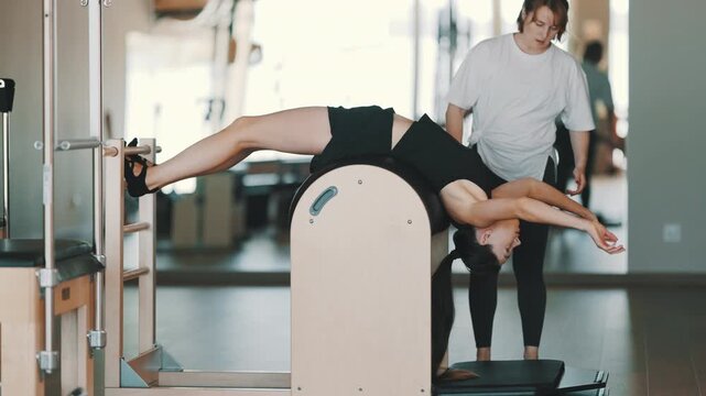 Pilates instructor guiding woman on ladder barrel equipment