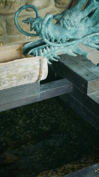 Vertical Close-up of Bronze Dragon Fountain Pouring Water into Bamboo Pipe at Japanese Shrine Chozuya