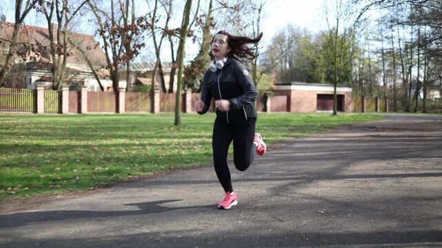 Young woman runs in park with incorrect running form showing beginner mistakes imbalance awkward posture learning process fitness training outdoor routine