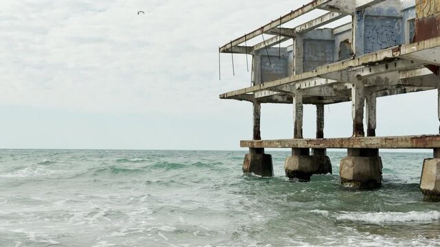 A skeletal, abandoned building stands over the crashing ocean. The crumbling concrete and gray sky create a lonely, haunting atmosphere. It feels like a quiet ghost of the past by the water.