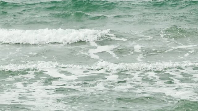 Foamy white waves roll across the emerald green water of the Black Sea. The repetitive motion of the sea creates a peaceful, rhythmic feeling. This view captures the raw energy of the ocean shore.