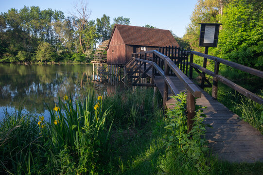 View of a charming old wooden mill house, its reflection shimmering on the still waters surrounded by vibrant green foliage, Tomasikovo, Trnava Region, Slovakia.