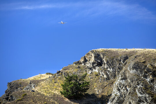 View of a passenger aircraft soaring above a rugged, rocky landscape on its approach to Queenstown Airport, Kawarau Gorge, Central Otago, New Zealand.