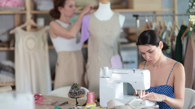 In workshop, woman employee dressmaker works with mannequin and future dress. Fashion designer makes clothes for customer. Female apprentice sew with sewing machine