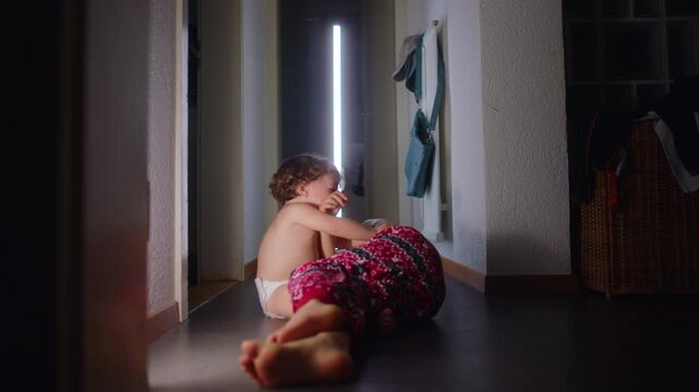 Toddler pulls older sibling clothes while playing on floor in home corridor, candid interaction showing curiosity, affection and lively sibling bond in everyday family life