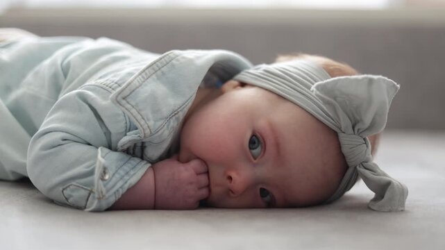 Adorable baby girl in denim jacket and headband resting on a soft surface