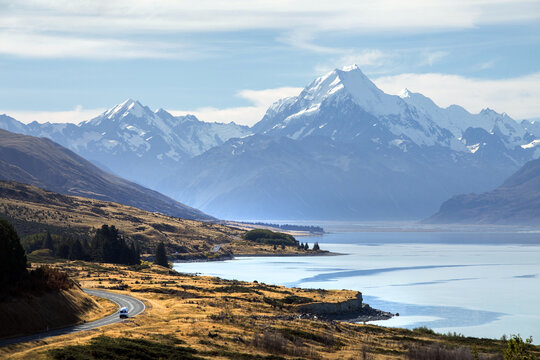 View of a camper van passing the crisp blue waters of Lake Pukaki, with Aoraki Mount Cook in the near distance, New Zealand.