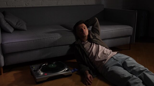 Young man relaxing on the floor next to a turntable, listening to vintage vinyl records in a dimly lit living room, finding solace and peace in the analog sound