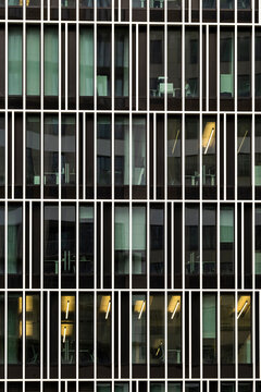 Modern architecture facade with glass windows reveals office corporate finance pattern and symmetry as interior lights glow behind a dark grid