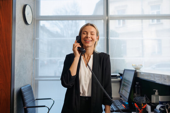 Happy female receptionist answering phone call at hotel reception counter