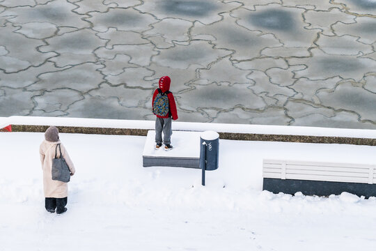 View of two figures, one in a striking red coat, stand near a frozen expanse, contrasting against the stark white snow-covered ground, Tallinn, Estonia.