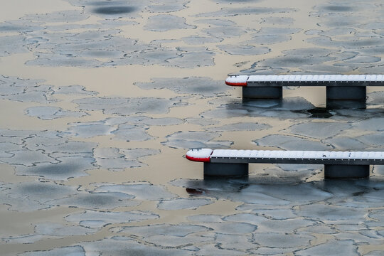 View of icy patterns dance on the water's surface, framing the stark white and grey docks with red accents in the winter light, Tallinn, Estonia.