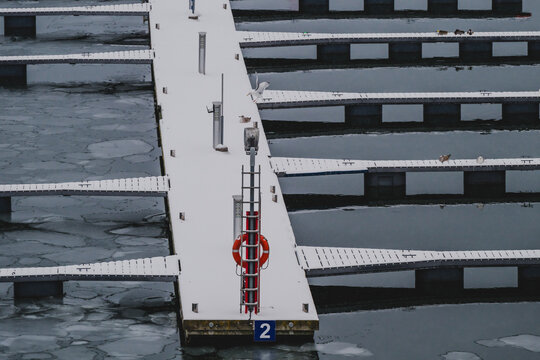 View of a snow-blanketed dock pierces the icy waters, a stark contrast of white and blue, with a vibrant red life preserver adding a splash of color, Tallinn, Estonia.