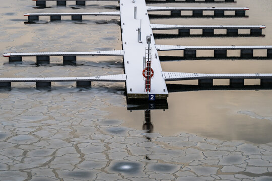 View of a stark white dock pierces through a mosaic of cracked ice on the water's surface, creating a serene yet contrasting winter scene, Tallinn, Estonia.
