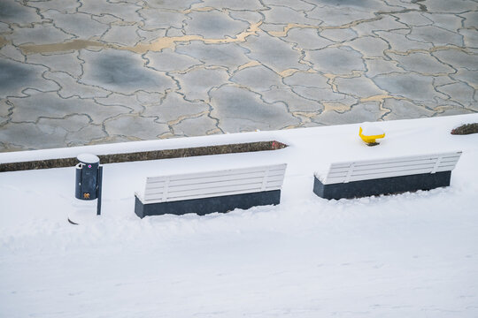 View of snow-covered benches and a whimsical yellow object contrast against the icy, fractured sea in the stark winter landscape, Tallinn, Estonia.