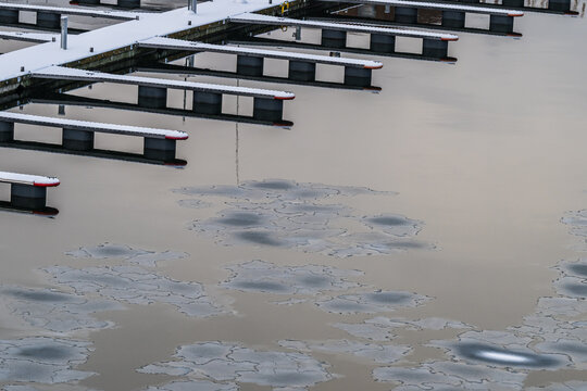 View of icy water speckled with floating ice formations reflecting the muted winter sky near a snow-dusted dock, Tallinn, Estonia.