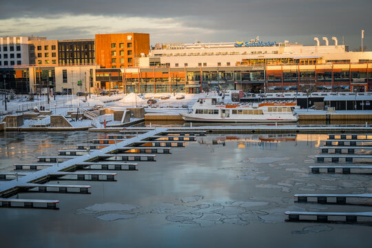 Tallinn, Estonia - 04 January 2025: View of a serene winter marina, icy waters and snow-dusted docks contrasting with modern buildings and the Tallink terminal.