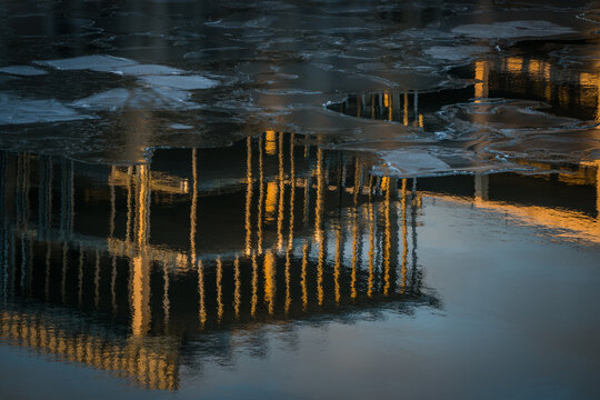 View of golden reflections shimmering on a half-frozen, dark body of water, broken ice floating like scattered jewels, a cold winter scene, Tallinn, Estonia.