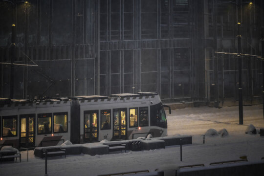 View of a modern tram glides through the snowy cityscape, its bright interior lights contrasting with the muted tones of the surrounding buildings, Tallinn, Estonia.