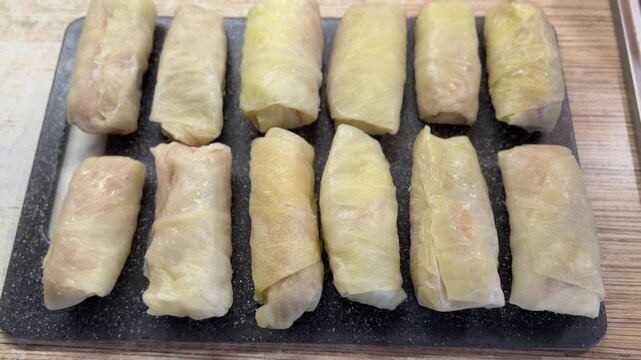 Cabbage rolls on black cutting board closeup, uncooked meat filled cabbage leaves rolled into neat cylinders, arranged in rows