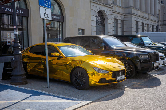 Warsaw, Masovian Voivodeship, Poland - April 25, 2026: A striking gold chrome Maserati Ghibli parked on a sunny street alongside a black Rolls-Royce Cullinan.