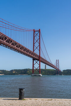 Lisbon, Portugal - 29 April 2022: View of the deep red 25 de Abril Bridge over the Tagus River, set against a brilliant blue sky, with Cristo Rei on the far bank.