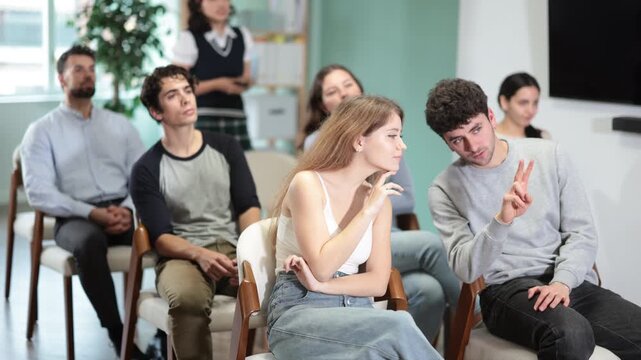  Female lecturer communicates with students, controls projector using remote control. Young people are listening to lecture in auditorium. Personal growth courses, practical classes in psychology