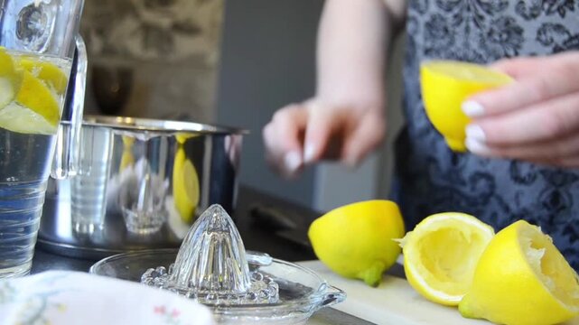 Close-up of hands squeezing fresh lemon using a manual juicer with juice dripping and splashing. Natural kitchen scene with citrus preparation and healthy drink concept.