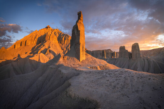 View of stark rock formations glowing with the warm hues of the setting sun against a dramatic skyline, casting long shadows, Hanksville, Utah, United States.