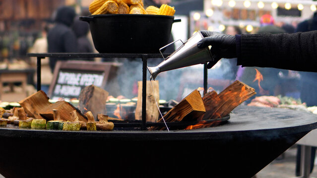 Grilling at a fair. Drizzling oil over the grilling surface. Grilled vegetables, wood fire in the center.