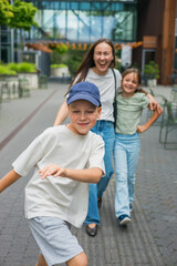 Obraz premium Happy laughing family having fun together outdoors on a casual summer day walking along a city pedestrian street with son in a cap in the foreground