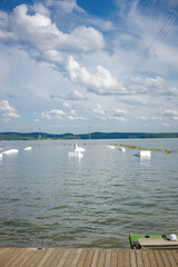 Fototapeta premium Empty wakeboarding park on a wide lake with white ramps and kickers under a blue sky with fluffy clouds seen from a wooden pier on a bright summer day