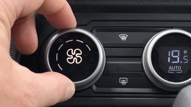 Close up of hand increasing car air conditioner fan speed using control knob, adjusting climate system, temperature set to auto, modern vehicle interior detail