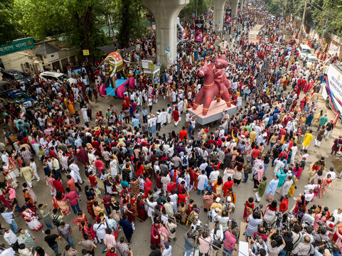 Dhaka, Bangladesh - 13 April 2026: Aerial view of a vibrant crowd celebrating a festival with large, colorful effigies under the grey concrete of an elevated structure.