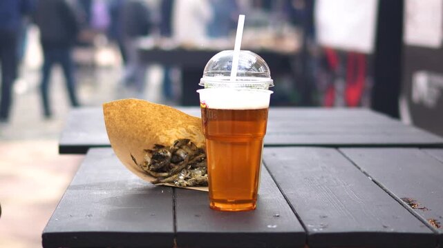 Delicious fried fish at the fair. Beer and fish in a bag on the table. Small dried fish for a snack.