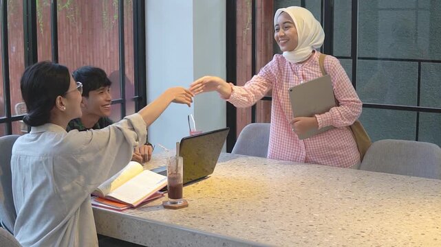 Asian woman hands over document to seated students and colleague before friendly handshake and warm farewell, hijabwearing