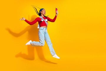 Fototapeta premium Joyful young woman jumping for a selfie against a bright yellow background