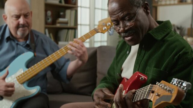 Close up shot of senior Black man playing electric guitar as beginner in music class for adults with teacher in background, active retirement concept