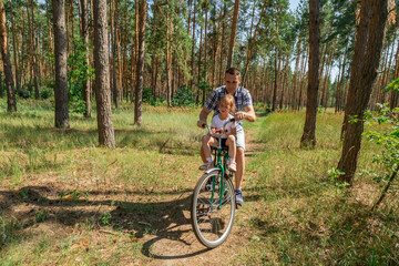 Fototapeta premium father riding a bike in summer forest with his baby daughter sitting in child seat