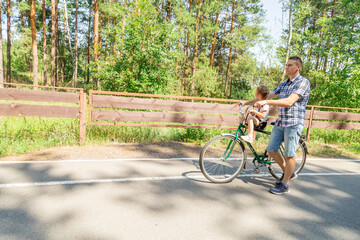 Obraz premium Young father with his little daughter on bicycle in summer sunny forest