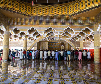 Tangail, Bangladesh - 21 March 2021: View of a large congregation of men praying, their reflections shimmering on the polished floor beneath ornate golden architecture.