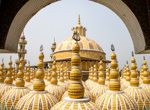 View of golden domes adorned with intricate patterns rise towards the sky, framed by an ornate archway, in Tangail, Dhaka Division, Bangladesh.